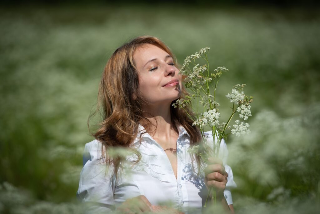 A woman with eyes closed holds wildflowers in a sunny field, embracing nature.