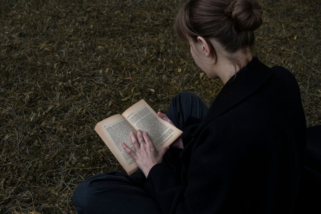 A young woman sits in an outdoor area reading a book, showcasing a peaceful moment of literature in nature.