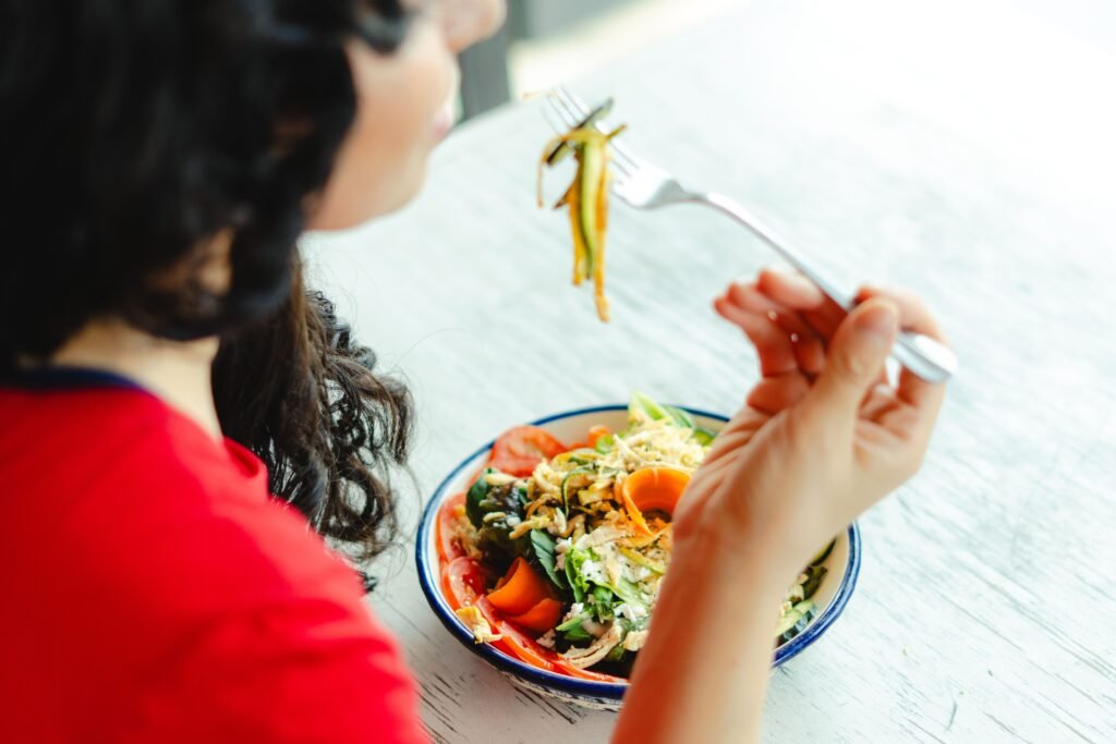 A woman in a red shirt enjoys a fresh salad indoors at a restaurant table.