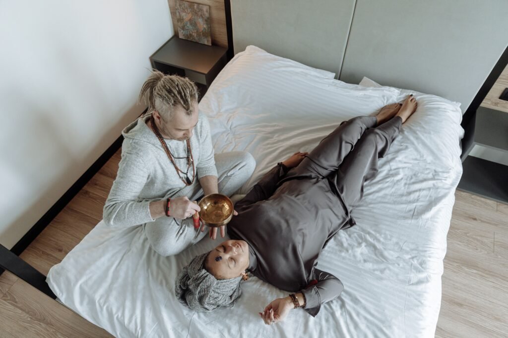 A man and woman involved in a spiritual healing session with a singing bowl on a bed.
