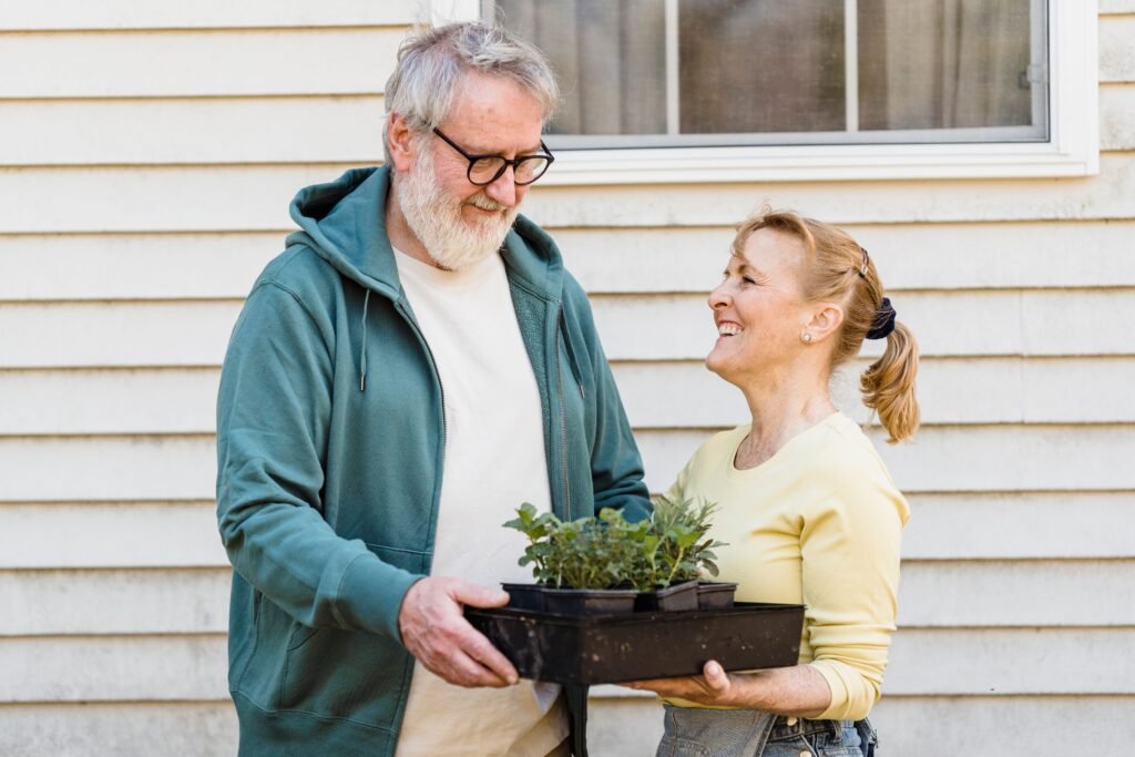 Happy elderly couple enjoying gardening, sharing moments while holding potted plants.