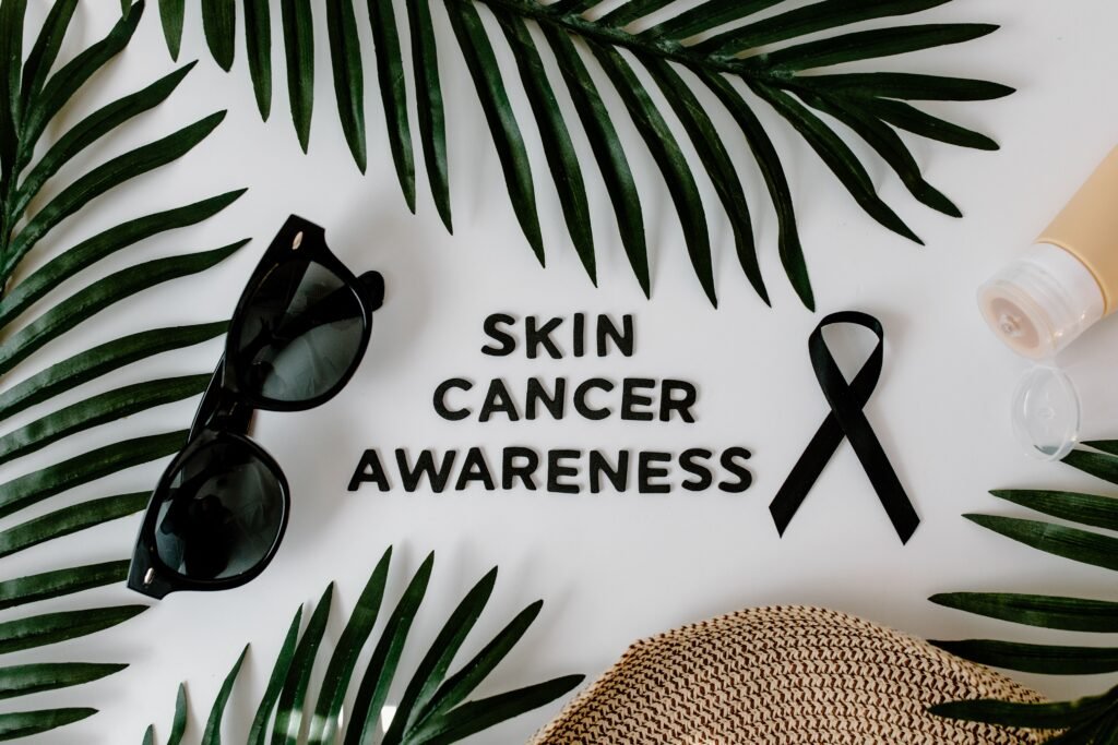 Flat lay image featuring palm leaves, sunglasses, a black ribbon, and skincare tube symbolizing skin cancer awareness.