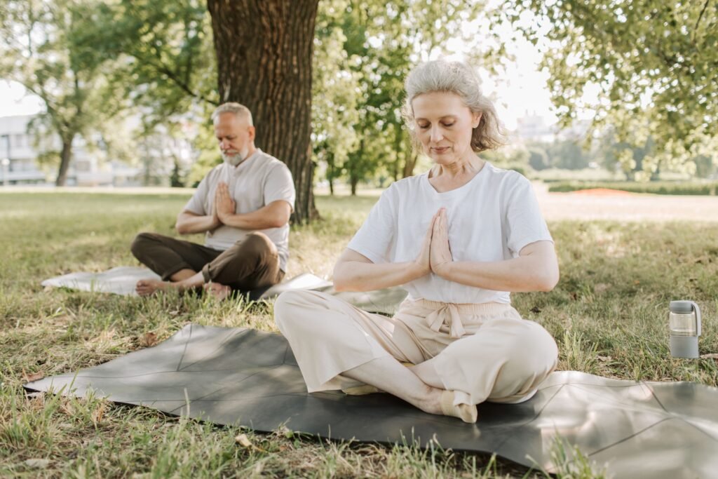Elderly couple practicing yoga meditation outdoors, focusing on health and tranquility.