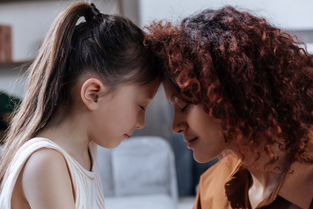 A touching moment between a mother and daughter with foreheads together indoors.