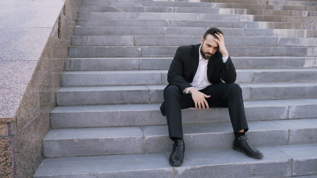 Businessman in a suit sitting distressed on concrete stairs, facing challenges.