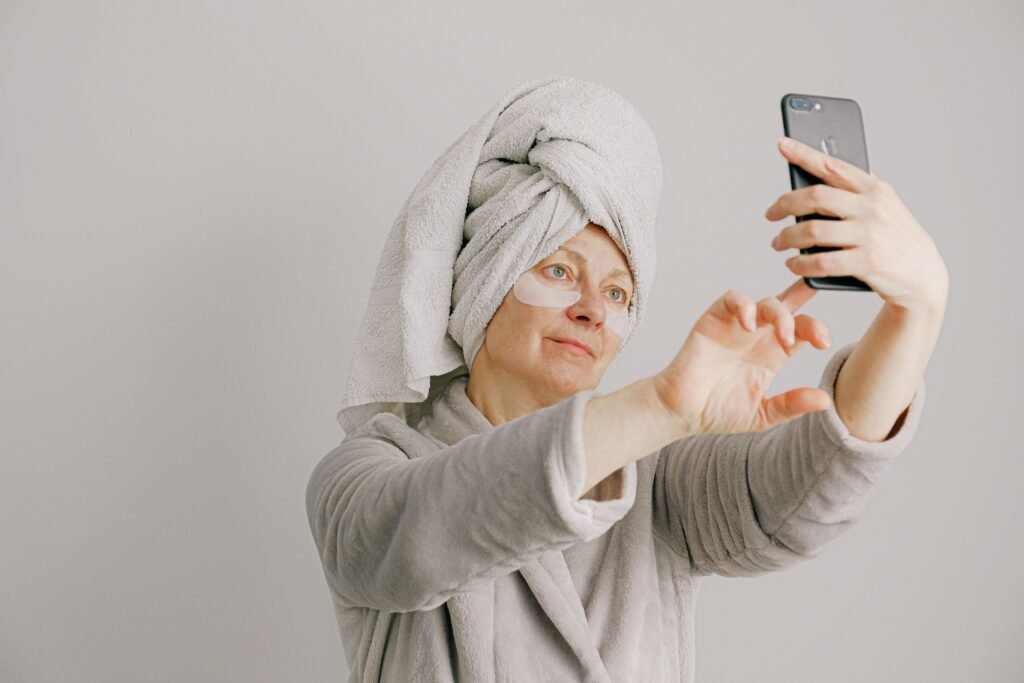 Woman in a bathrobe with skincare pads taking a selfie, promoting self-care and relaxation.