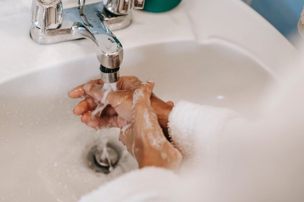 High angle of crop anonymous ethnic female washing hands with foamy water during morning hygiene routine